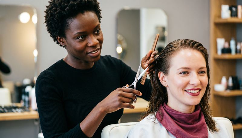 Une coiffeuse coupe les cheveux d’une cliente dans son salon